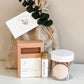 A curated gift set featuring a bar of oatmeal milk and honey soap in a kraft box, a small roller bottle, a clear jar of dried botanicals with a white lid, and a burlap drawstring bag with a white card and eucalyptus sprig, all on a light surface against a neutral beige background.